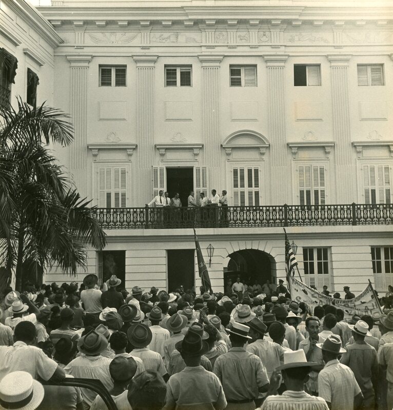 Gob. Piñero y otros oficiales en balcón de La Fortaleza, obreros reunidos.